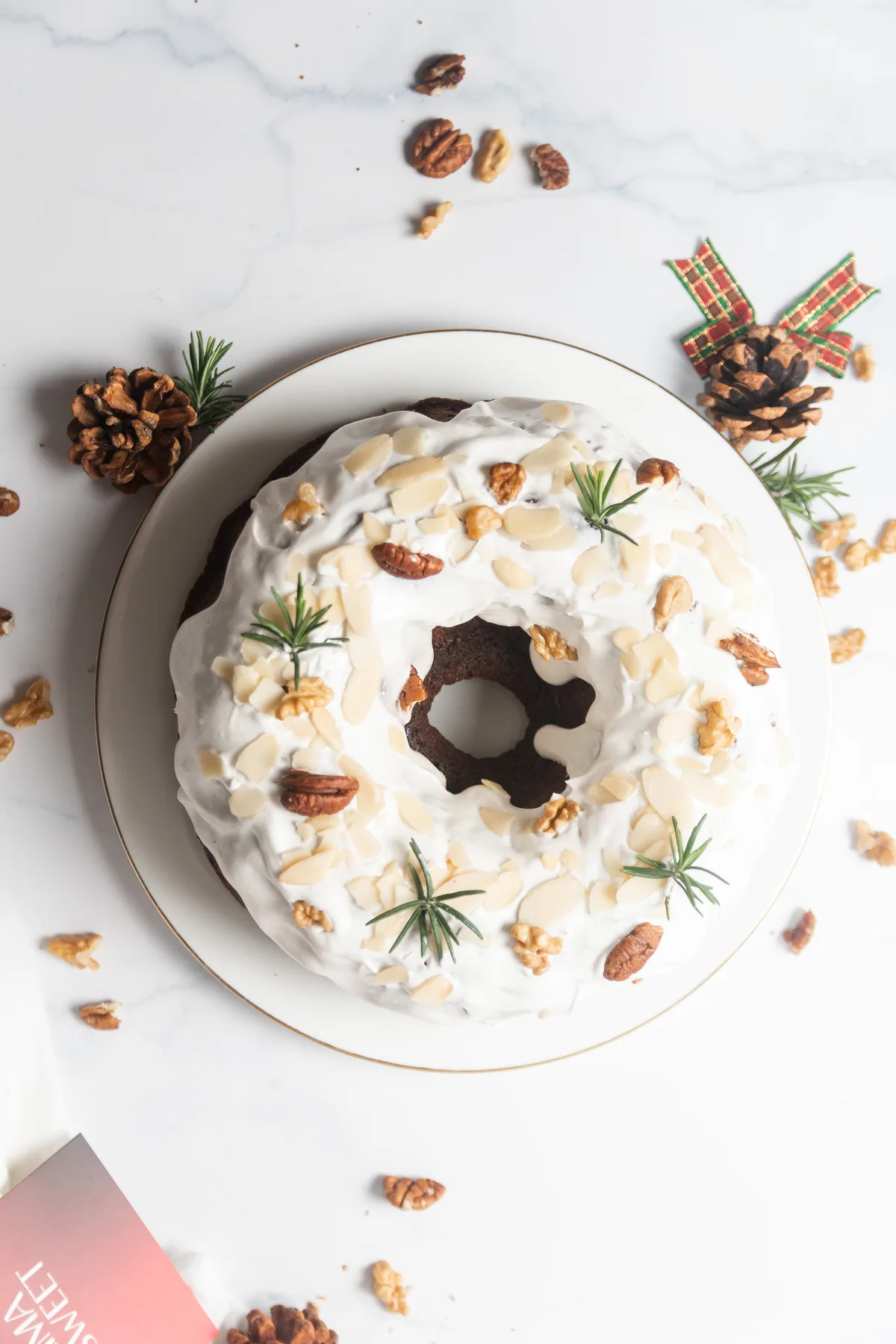 Bundt cake navideño con glaseado blanco, nueces y romero, piñas decorativas de fondo