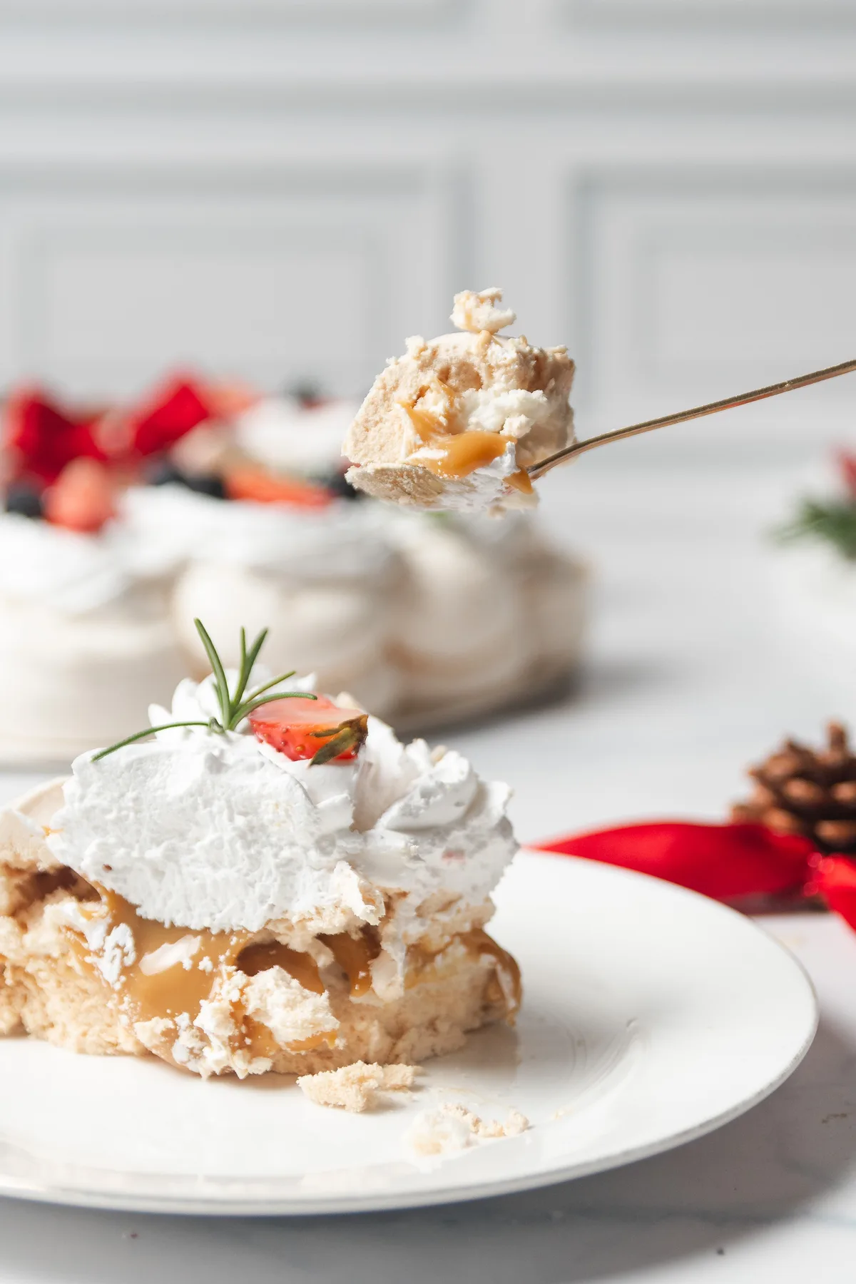 Cuchara levantando un bocado de pavlova con caramelo goteando, en su ambientación navideña