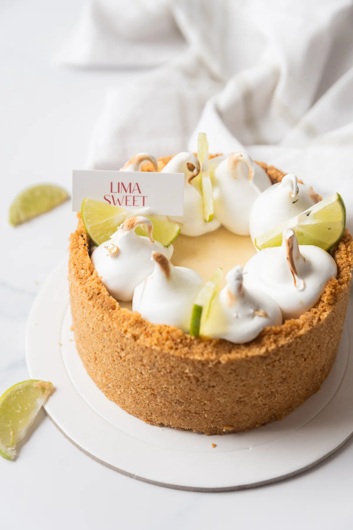 Pie de limón en formato de torta entera, con merengues y rodajas de lima, tarjeta de marca
