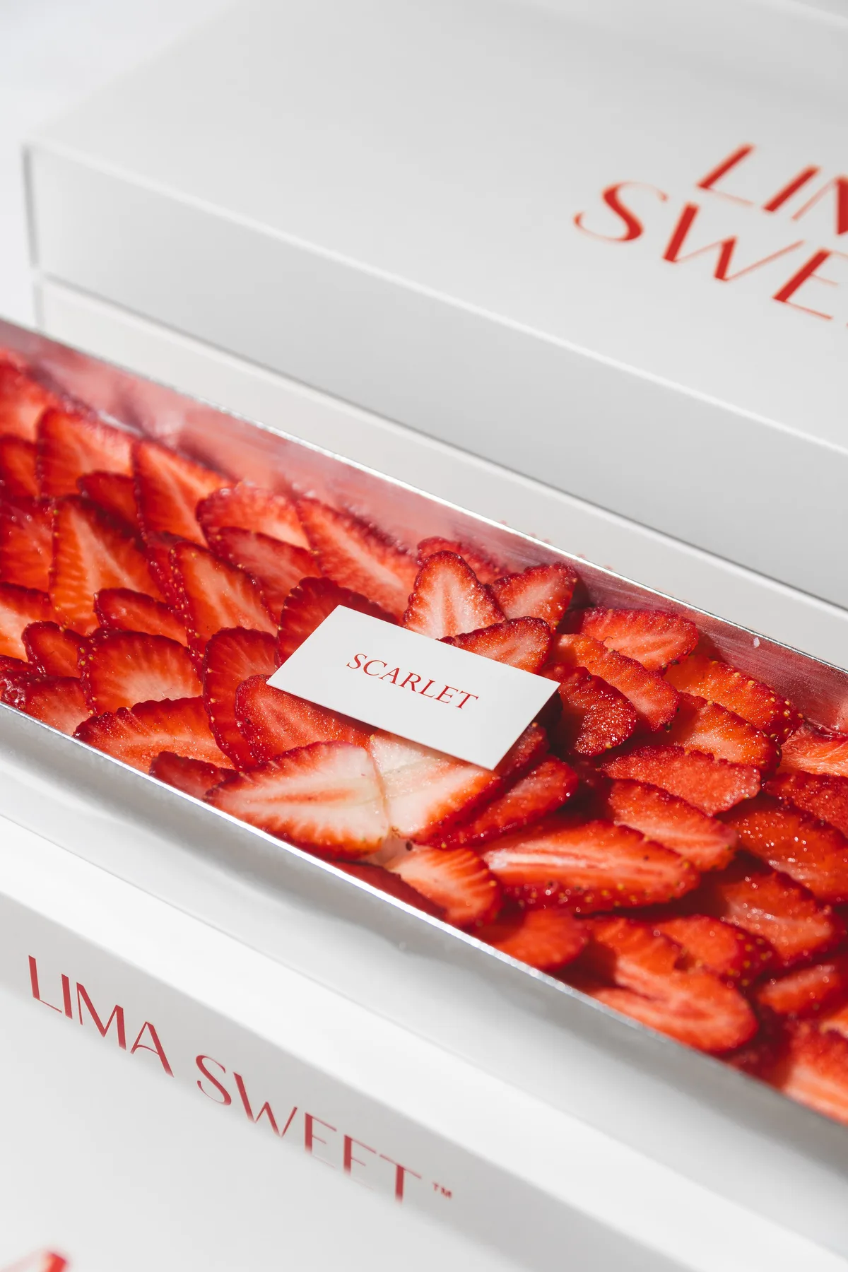 Fresas laminadas en abanico sobre bandeja plateada, junto a la tarjeta Scarlet de Lima Sweet