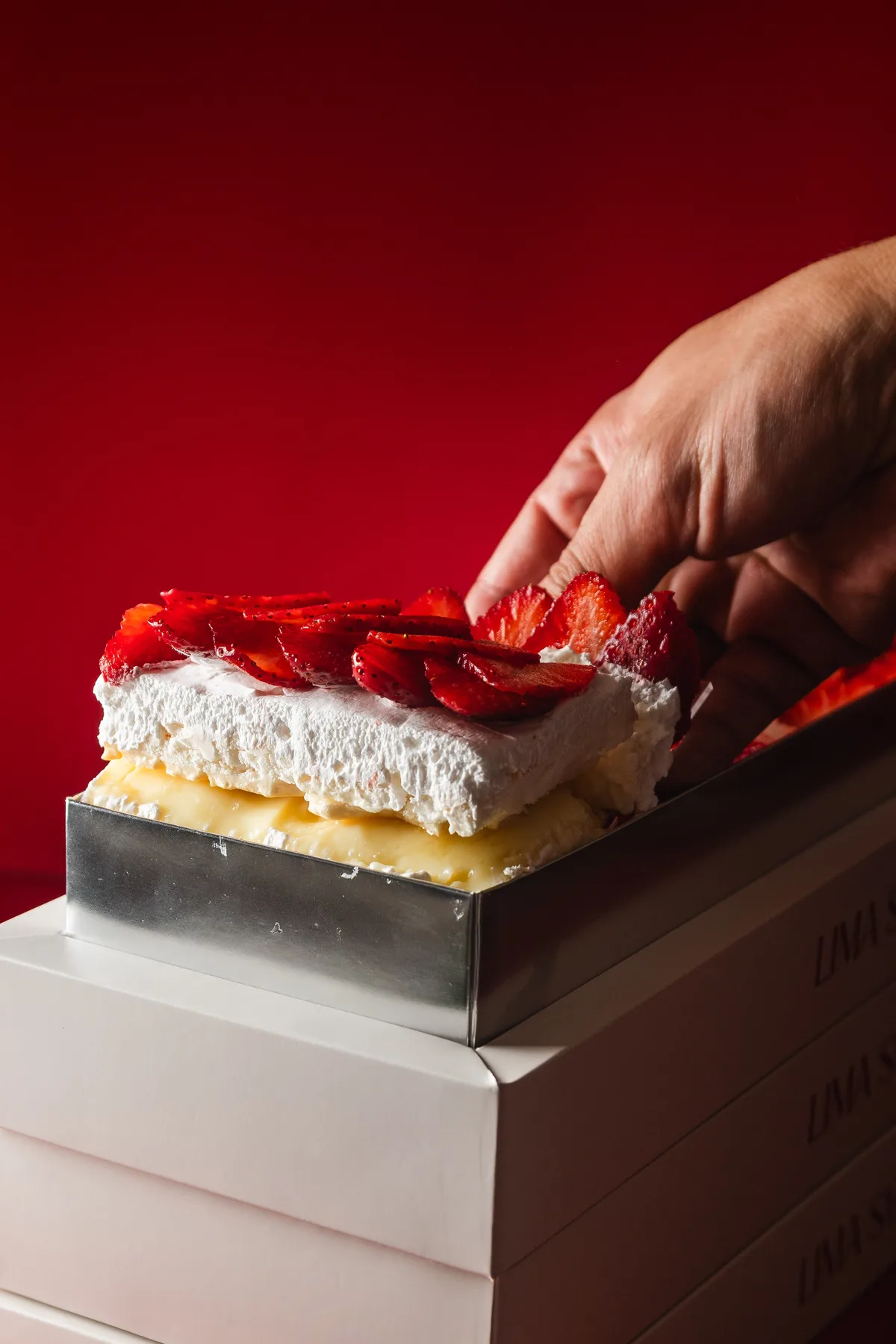 Mano colocando fresas sobre las capas de bizcocho, crema pastelera y chantilly